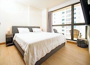 Une chambre d’hôtel moderne, dotée d’un grand lit, d’une table de chevet, d’une chaise et offrant une vue sur la ville grâce à de grandes fenêtres.