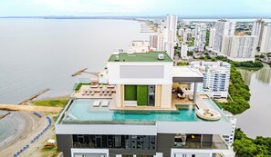 Un immeuble de grande hauteur doté d’une piscine sur le toit, d’un espace aménagé comme une plage et offrant une vue sur la mer.