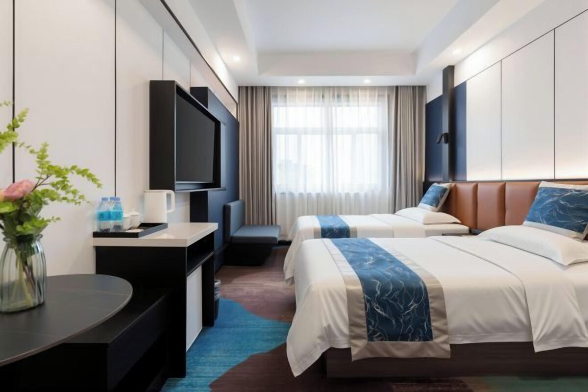 Habitación de hotel con dos camas, televisión, escritorio y ventana con cortinas.