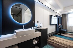 Un baño de hotel moderno con un espejo redondo, un lavabo, tocador y televisión.