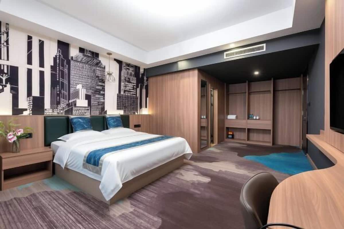 Une chambre d’hôtel moderne, dotée d’un grand lit, d’un bureau, d’une télévision et d’une fresque murale représentant un paysage urbain.