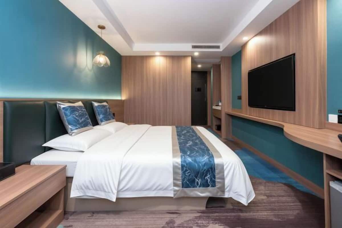 Une chambre d’hôtel moderne dotée d’un grand lit, d’un téléviseur à écran plat fixé au mur et d’une tête de lit en bois.