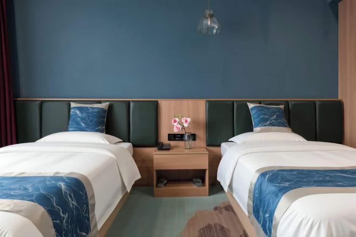 Une chambre d’hôtel avec deux lits, une table de chevet avec une lampe et un luminaire fixé au mur.