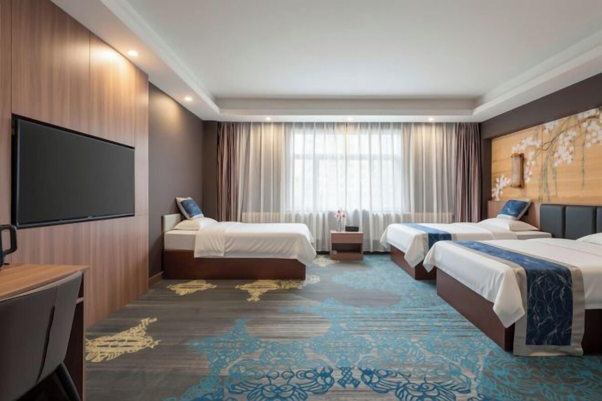 Habitación de hotel con dos camas, televisión, escritorio y un ventanal con cortinas.