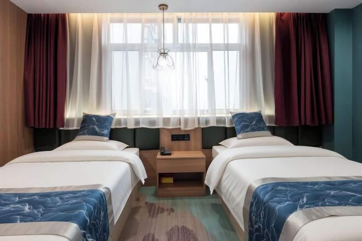 Une chambre d’hôtel avec deux lits, une table de chevet, une fenêtre avec des rideaux et une tête de lit en bois.