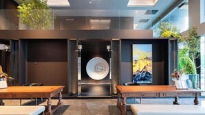 Un intérieur moderne avec un élément central circulaire, des tables en bois, des bancs et des plantes en pot.