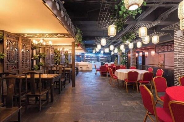 A restaurant with wooden tables and chairs, hanging lanterns, and a brick wall.