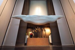 A reception area with a large white sculpture, a wooden reception desk, and a staircase leading to an upper level.
