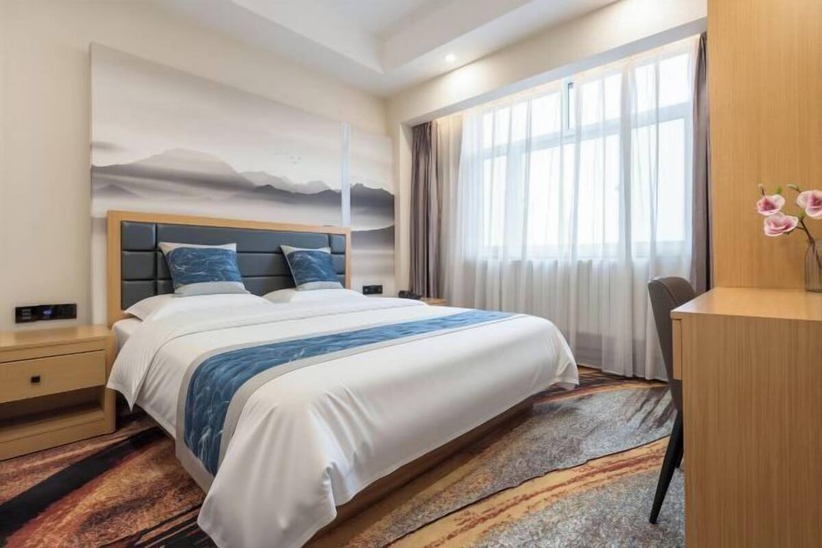 Une chambre d’hôtel avec un grand lit, un bureau, une table de chevet et une fenêtre avec des rideaux.