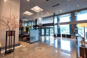 A spacious lobby with a modern design, featuring a reception desk, seating area, and large windows allowing natural light.