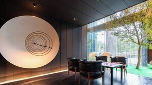 Un intérieur moderne avec un luminaire circulaire, un plancher en bois et une vue sur un arbre à travers de grandes fenêtres.
