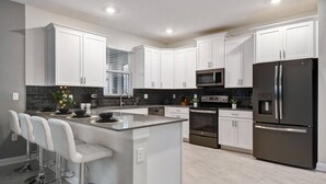 Una cocina moderna con armarios blancos, electrodomésticos de acero inoxidable y una isla central con taburetes de bar.