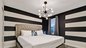 Un dormitorio con cabecera capitonada, una cama grande, una lámpara de araña moderna y paredes a rayas blancas y negras.