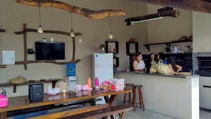 A rustic kitchen with a wooden ceiling, a television mounted on the wall, and a bar area with stools.