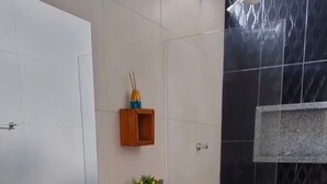 A bathroom with a white toilet, a granite countertop, a small wooden cabinet, a potted plant, and a shower area with black tiles.