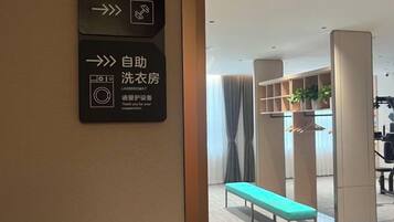 A hotel interior with a fitness room sign, a self-service laundry room sign, and a bench in the center.