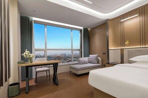 A modern hotel room with a large window, a sofa, a bed, a desk, and a view of the cityscape. - Phoenix Court Hotel (Jingzhou Ancient City Changjiang University) (Jingzhou)