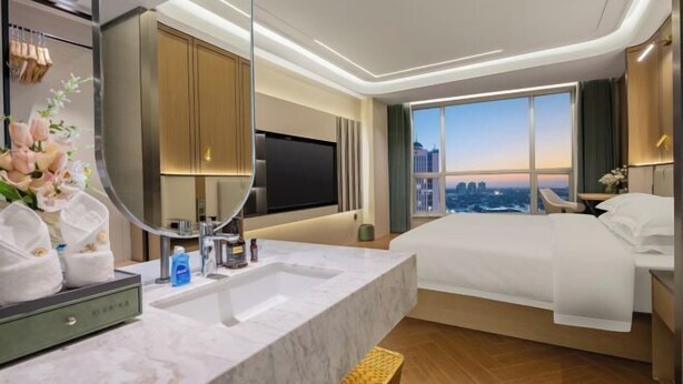 A modern hotel room with a large bed, a TV, a bathroom with a mirror, and a city view. - Phoenix Court Hotel (Jingzhou Ancient City Changjiang University) (Jingzhou)