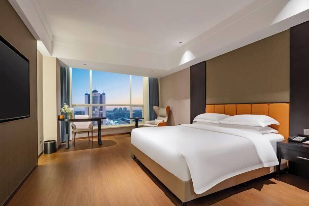 A modern hotel room with a large bed, a desk, and a view of the cityscape.