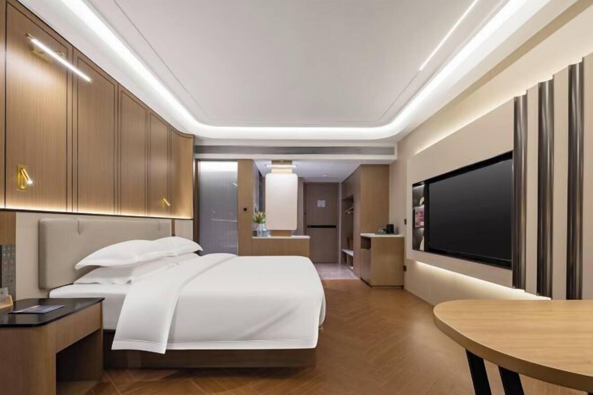 A modern hotel room with a large bed, bedside tables, a TV, and a dining area.