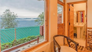 Una habitación con un ventanal amplio que da a un paisaje montañoso, una silla de madera y un baño con lavabo y espejo.