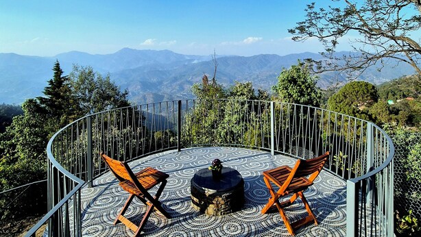 Un espacio de estar al aire libre con forma circular, suelo estampado y barandilla de metal, con vistas a un paisaje montañoso.