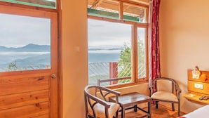 Una habitación con un escritorio de madera, dos sillas, una cama y una ventana que da a vistas de montañas.