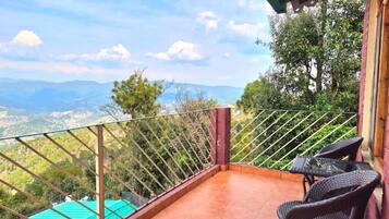 Un balcon avec vue sur les montagnes, une piscine et deux fauteuils en osier.