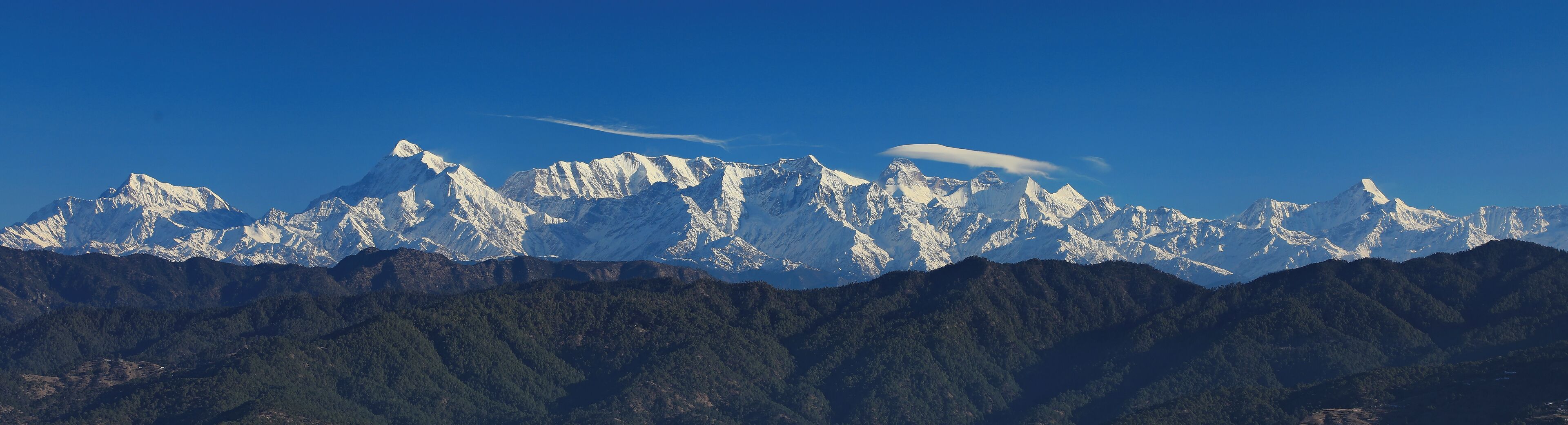 Una cordillera con picos nevados y valles cubiertos de bosques densos.