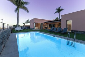 A swimming pool with lounge chairs, a patio area, and a building with large windows.