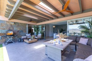 An open-plan living area with a stone wall, a grill, wicker furniture, and a view through a glass door.