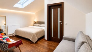 A bedroom with a bed, a sofa, a chair, a wooden floor, a door, and a skylight. - Loft Jecna 43 Prague (Prague)