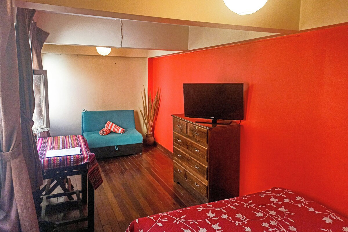 Una habitación con un sofá azul, un aparador de madera, un televisor encima y una pared roja.