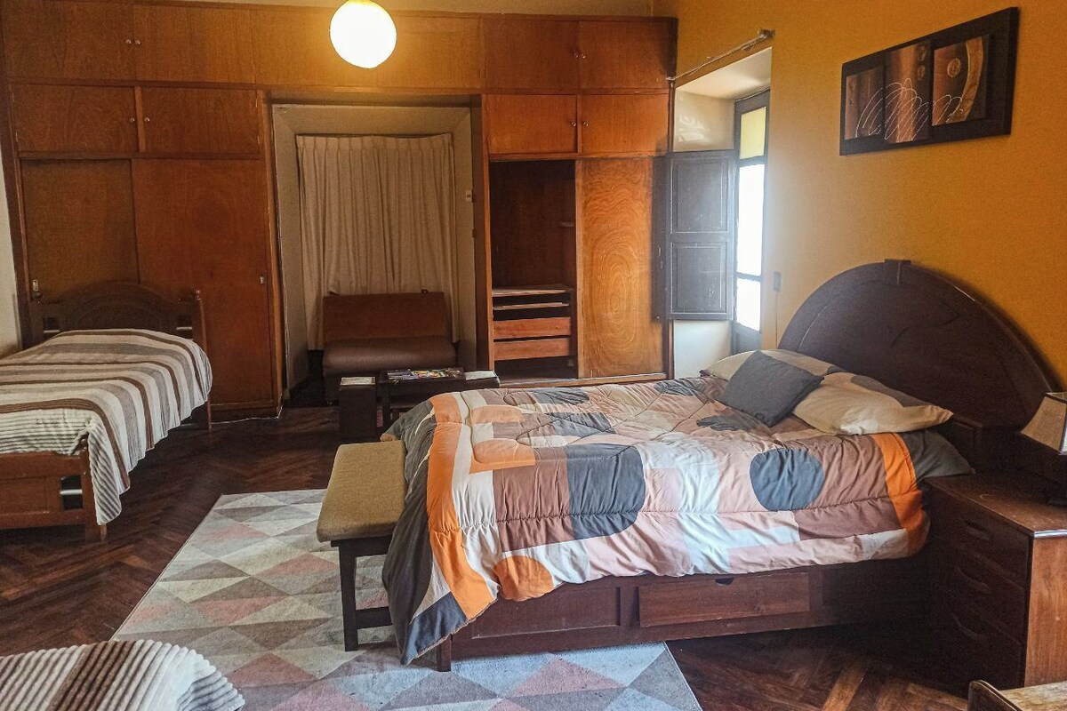 Une chambre à coucher avec un grand lit, un plus petit lit, un banc et une armoire.