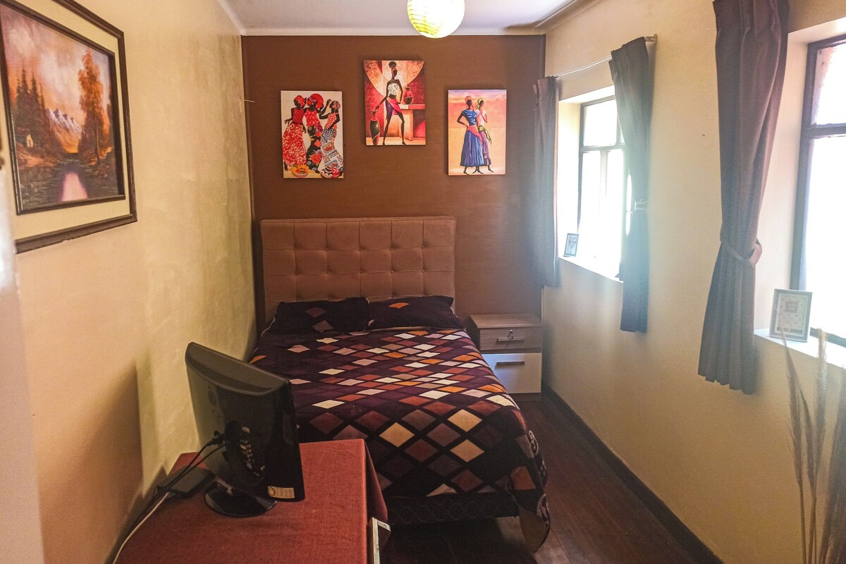 Une chambre avec un lit, un bureau et un ordinateur. Il y a trois tableaux accrochés au mur.