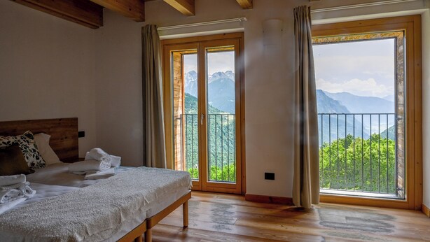 Une chambre à coucher avec un lit en bois, un banc et une vue sur les montagnes, visible à travers de grandes fenêtres.