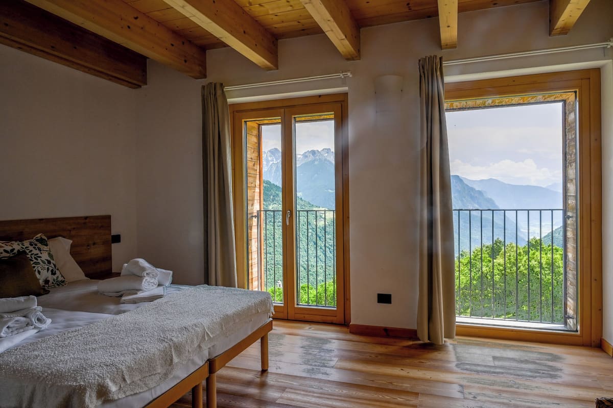 Een slaapkamer met een houten bed, een bankje en een uitzicht op bergen door grote ramen.