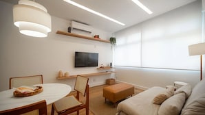 A modern living room with a flat-screen TV, wooden furniture, and a large window. - Leblon | 5min to Beach & Perfect Location (Rio de Janeiro)