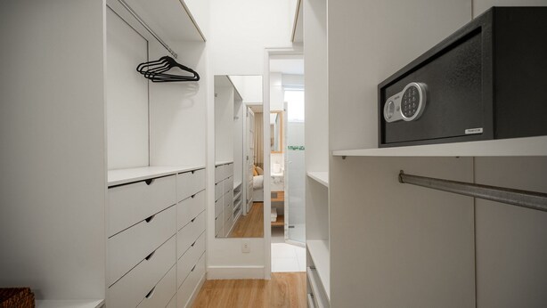 A narrow hallway with white storage cabinets, a black safe, and a wooden floor. - Leblon | 5min to Beach & Perfect Location (Rio de Janeiro)
