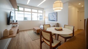 A modern dining area with a round table, wooden chairs, and a hanging light fixture. - Leblon | 5min to Beach & Perfect Location (Rio de Janeiro)
