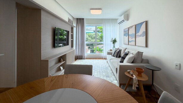 A modern living room with a TV, a sofa, a dining table, and a view of the outdoors.
