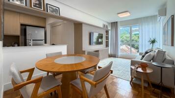 Un espace de vie moderne comprenant une table à manger en bois, des chaises, un canapé, une petite table d’appoint et un coin cuisine avec un réfrigérateur.