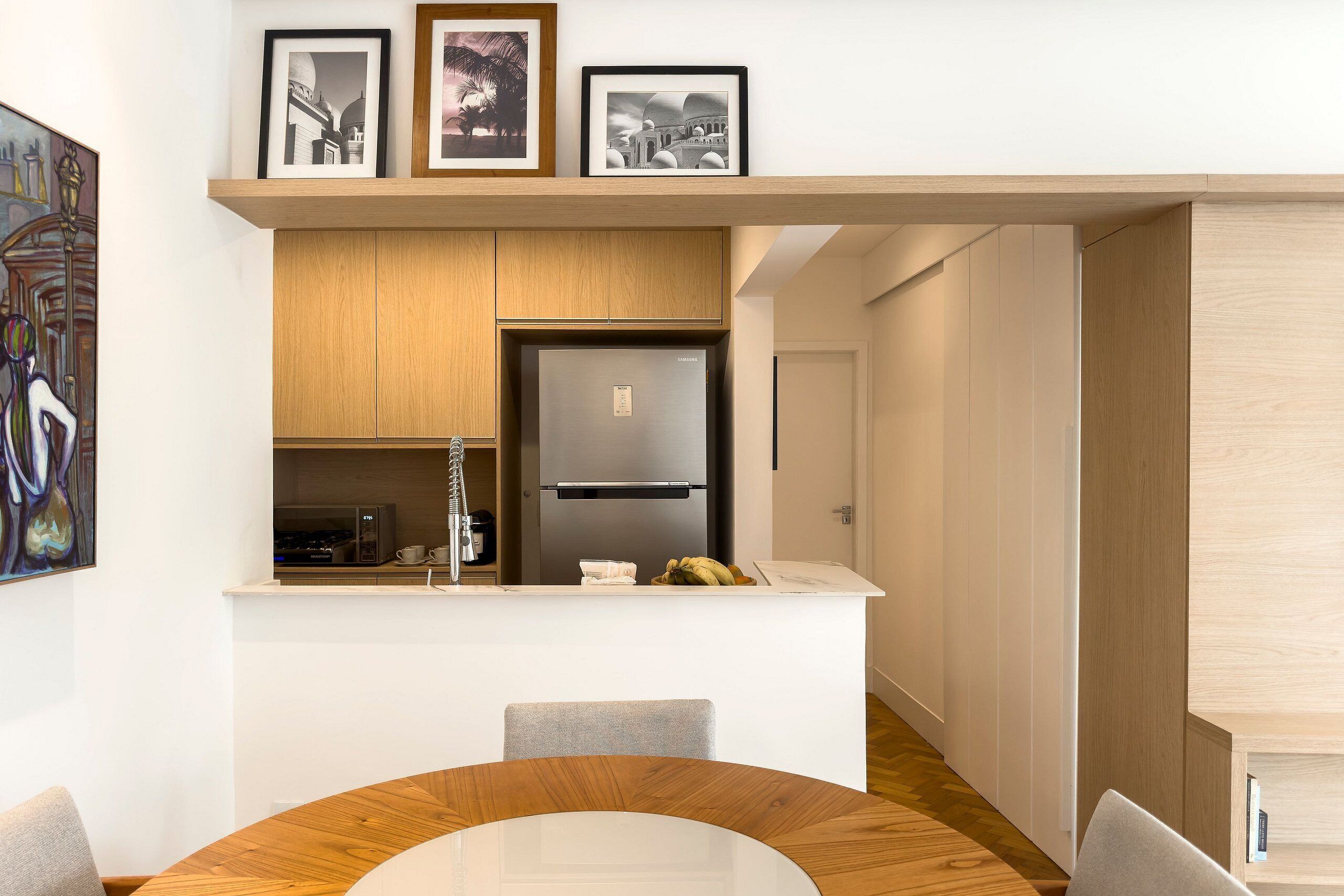 Een moderne keuken met een inbouwkoelkast, houten kasten, en een eethoek met een ronde tafel en stoelen.