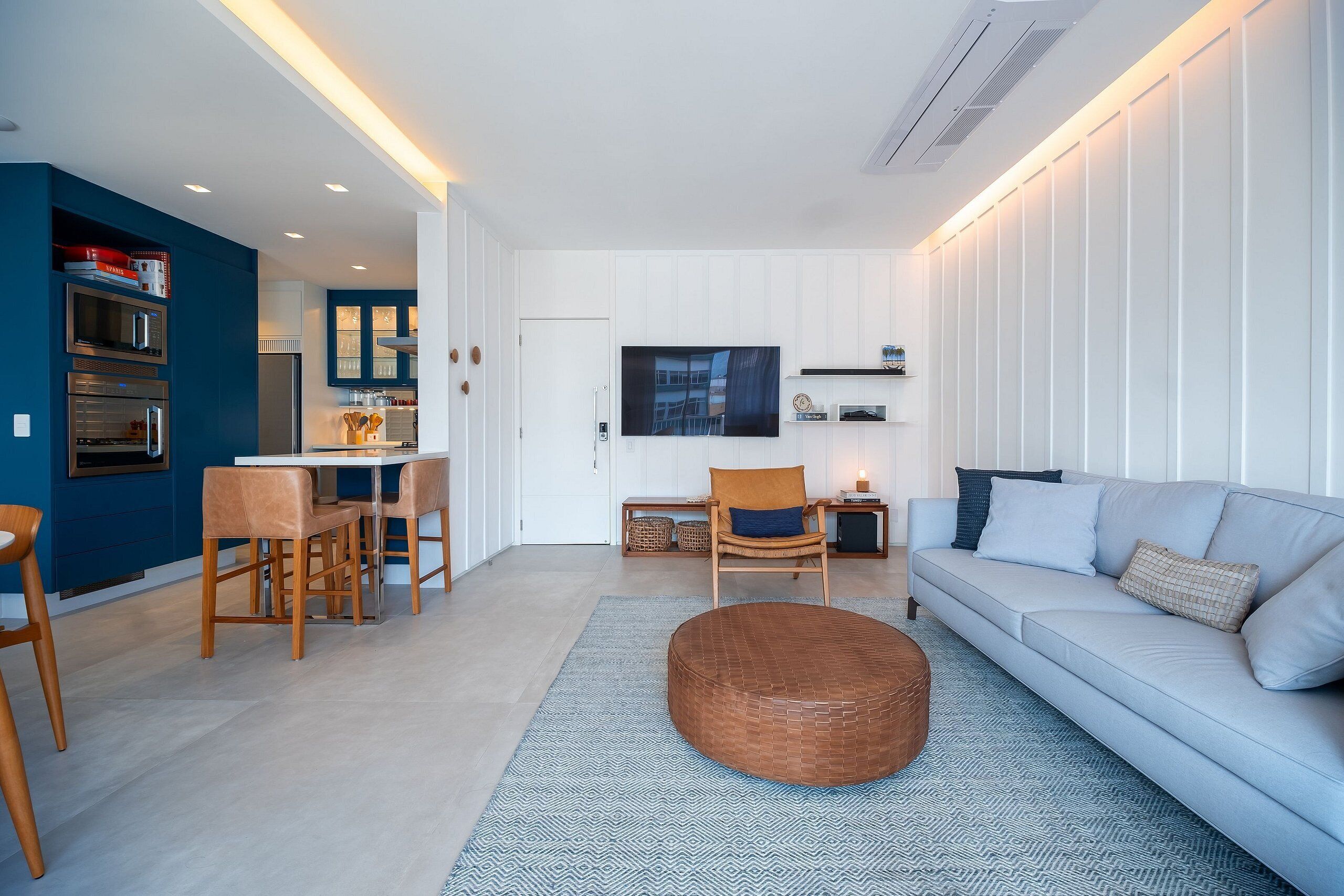 Een moderne woonkamer met een bank, stoelen, een salontafel en een keuken met apparatuur.