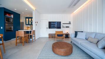 Een moderne woonkamer met een bank, stoelen, een salontafel en een keuken met apparatuur.