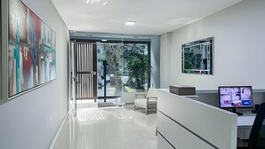A modern reception area with a glass door leading to a balcony, a desk with a computer, and a large abstract painting on the wall. - Leblon | 3 dorms | 6 minutes from the beach (Rio de Janeiro)