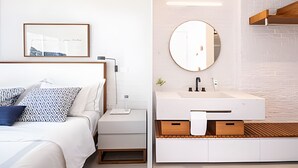 A modern bedroom with a bed, bedside table, and a framed picture on the wall. The image also shows a bathroom with a sink, mirror, and wooden storage. - Leblon | 3 dorms | 6 minutes from the beach (Rio de Janeiro)