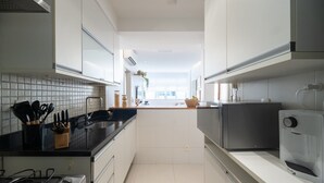 A modern kitchen with white cabinets, a black countertop, and stainless steel appliances. - Impeccable apartment in a great location in Leblon (Rio de Janeiro)