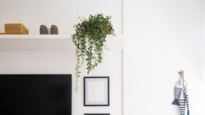 A modern living room with a flat-screen TV, framed artwork, a hanging plant, and a wooden bench. - Impeccable apartment in a great location in Leblon (Rio de Janeiro)