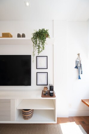 Een moderne woonkamer met een flatscreen televisie, kunstwerken in lijsten, een hangplant en een klein houten tafeltje met een mand.